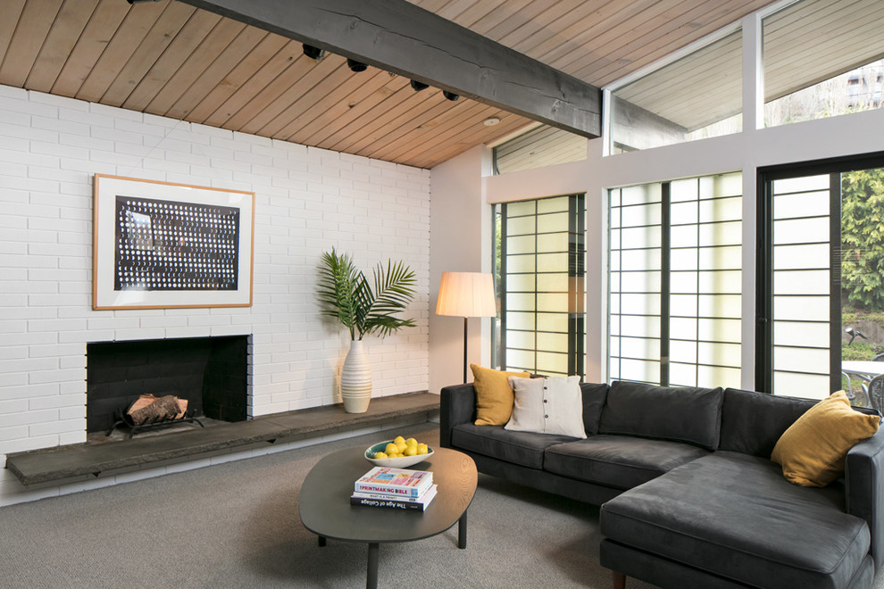 This is an example of a small midcentury open concept family room in Seattle with white walls, carpet, a standard fireplace, a brick fireplace surround, a corner tv and grey floor.