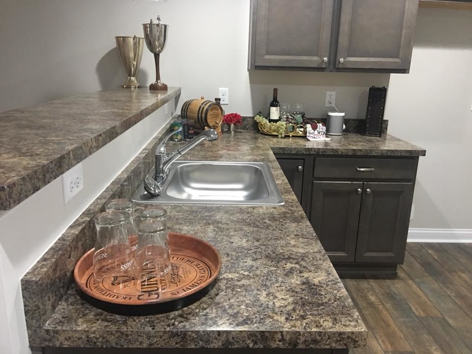 This is an example of a mid-sized transitional l-shaped home bar in Cincinnati with a drop-in sink, recessed-panel cabinets, dark wood cabinets, laminate benchtops, dark hardwood floors, brown floor and brown benchtop.