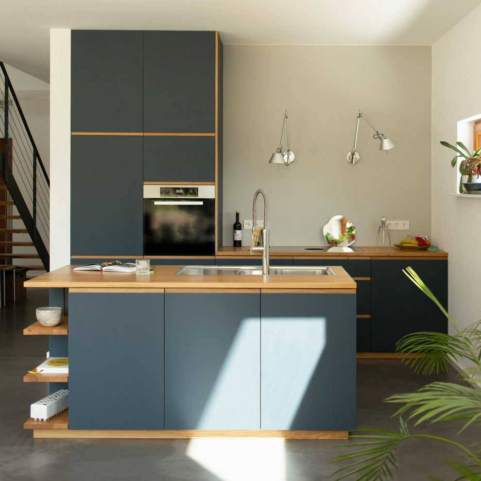 Идея дизайна: параллельная кухня-гостиная среднего размера в современном стиле с плоскими фасадами, синими фасадами, деревянной столешницей, бетонным полом, островом, серым полом и коричневой столешницей