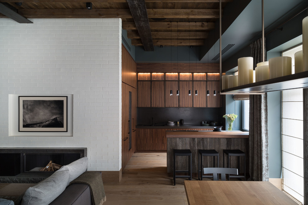 This is an example of a mid-sized industrial l-shaped open plan kitchen in Moscow with medium wood cabinets, quartzite benchtops, flat-panel cabinets, black splashback, light hardwood floors, beige floor, black benchtop and a peninsula.