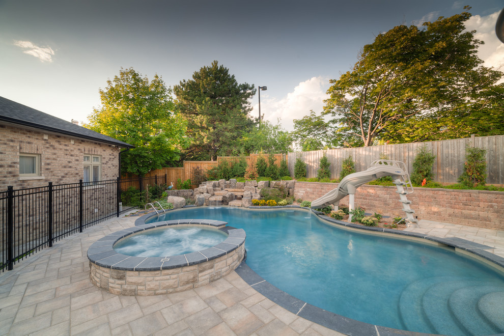 Design ideas for a large traditional backyard custom-shaped pool in Toronto with a water slide and brick pavers.