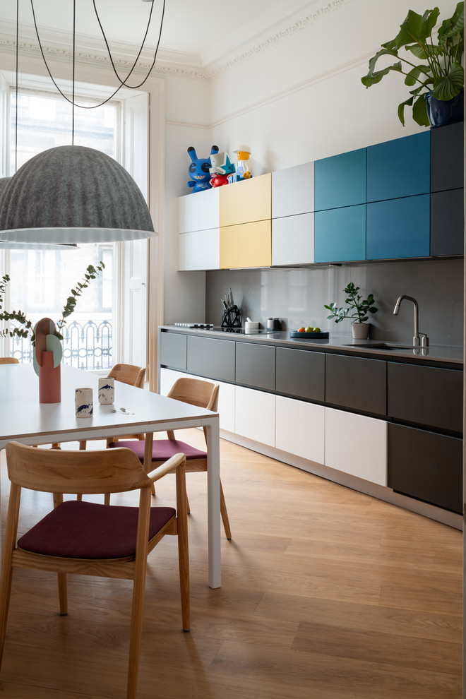 This is an example of a mid-sized contemporary single-wall eat-in kitchen in Edinburgh with flat-panel cabinets, quartzite benchtops, grey splashback, stainless steel appliances, medium hardwood floors, no island, grey benchtop, an undermount sink and brown floor.