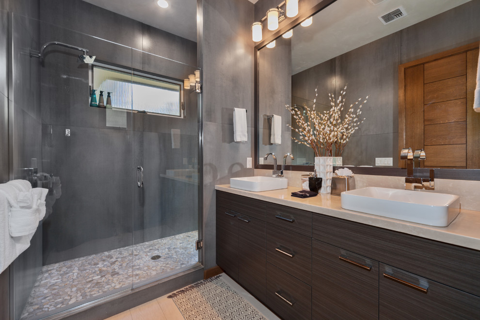 This is an example of a mid-sized contemporary master bathroom in Hawaii with porcelain floors, flat-panel cabinets, brown cabinets, an alcove shower, porcelain tile, grey walls, a vessel sink, limestone benchtops, beige floor and a hinged shower door.