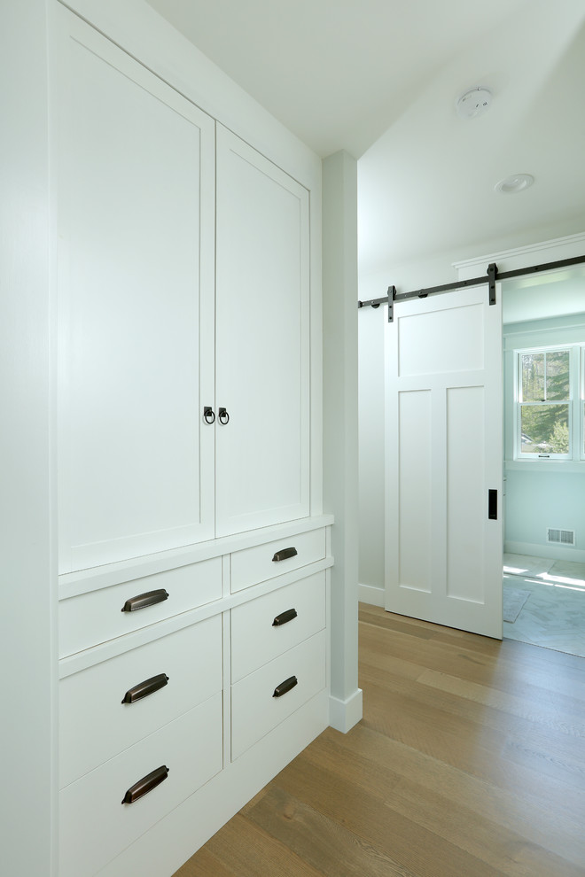 Design ideas for a small country gender-neutral built-in wardrobe in Grand Rapids with recessed-panel cabinets, white cabinets, light hardwood floors and brown floor.