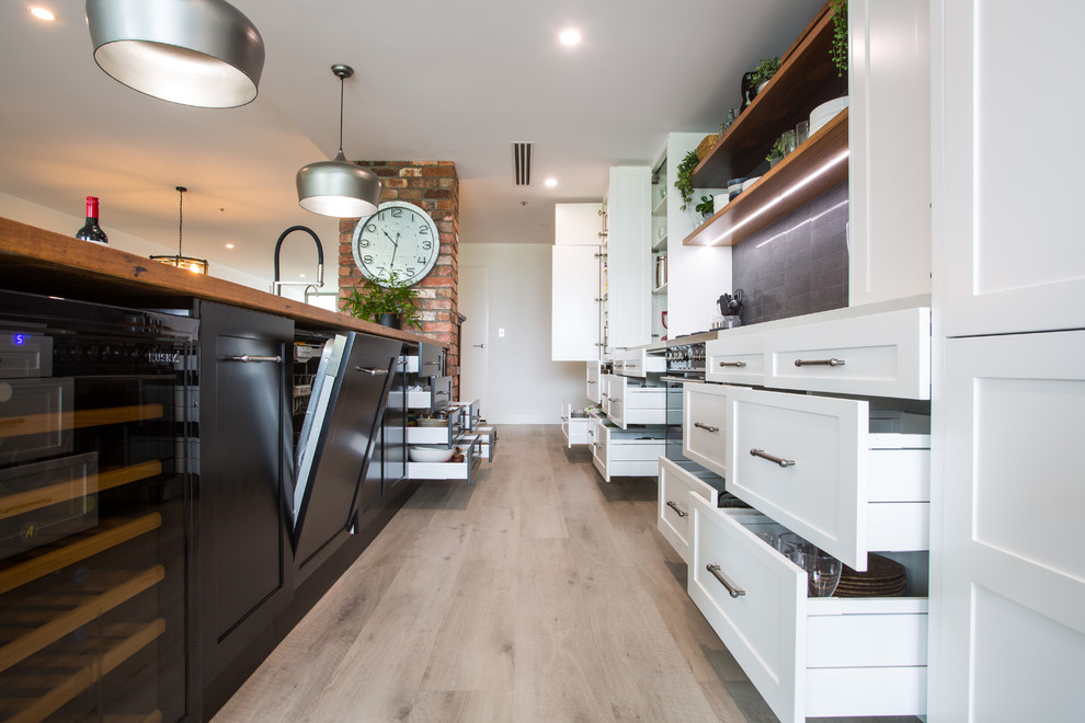 Expansive country galley eat-in kitchen in Brisbane with a double-bowl sink, recessed-panel cabinets, black cabinets, wood benchtops, black splashback, subway tile splashback, black appliances, with island, grey floor and white benchtop.