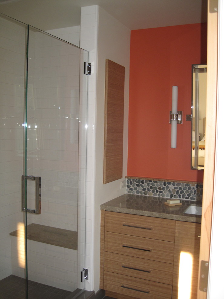 This is an example of a small contemporary master bathroom in San Francisco with an undermount sink, flat-panel cabinets, medium wood cabinets, limestone benchtops, an alcove shower, white tile, pebble tile, orange walls, ceramic floors and a one-piece toilet.