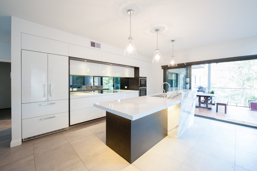 Photo of a large modern single-wall open plan kitchen in Melbourne with an undermount sink, flat-panel cabinets, white cabinets, quartz benchtops, metallic splashback, mirror splashback, black appliances, porcelain floors, with island and grey floor.