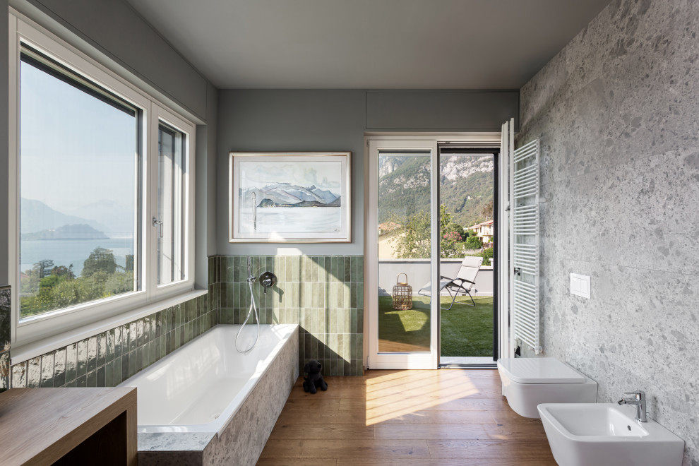 Exempel på ett stort modernt beige beige en-suite badrum, med släta luckor, vita skåp, ett platsbyggt badkar, en vägghängd toalettstol, grön kakel, stickkakel, gröna väggar, mellanmörkt trägolv, ett fristående handfat, träbänkskiva och beiget golv