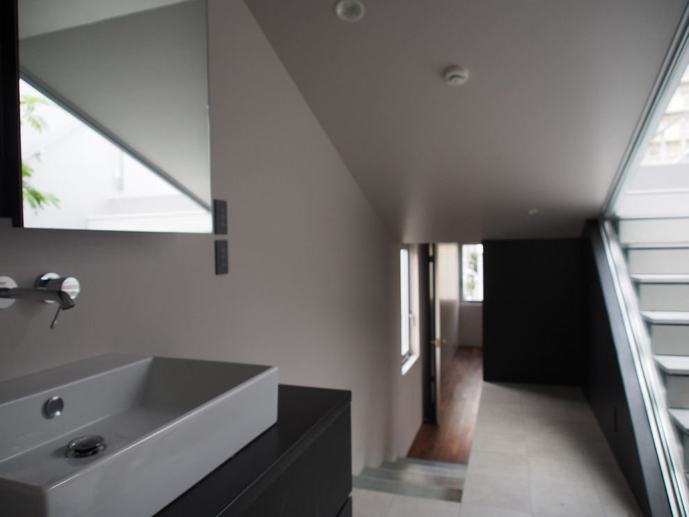 Modern powder room in Tokyo with flat-panel cabinets, black cabinets, a one-piece toilet, grey walls, ceramic floors, a vessel sink, solid surface benchtops, grey floor, black benchtops and a built-in vanity.