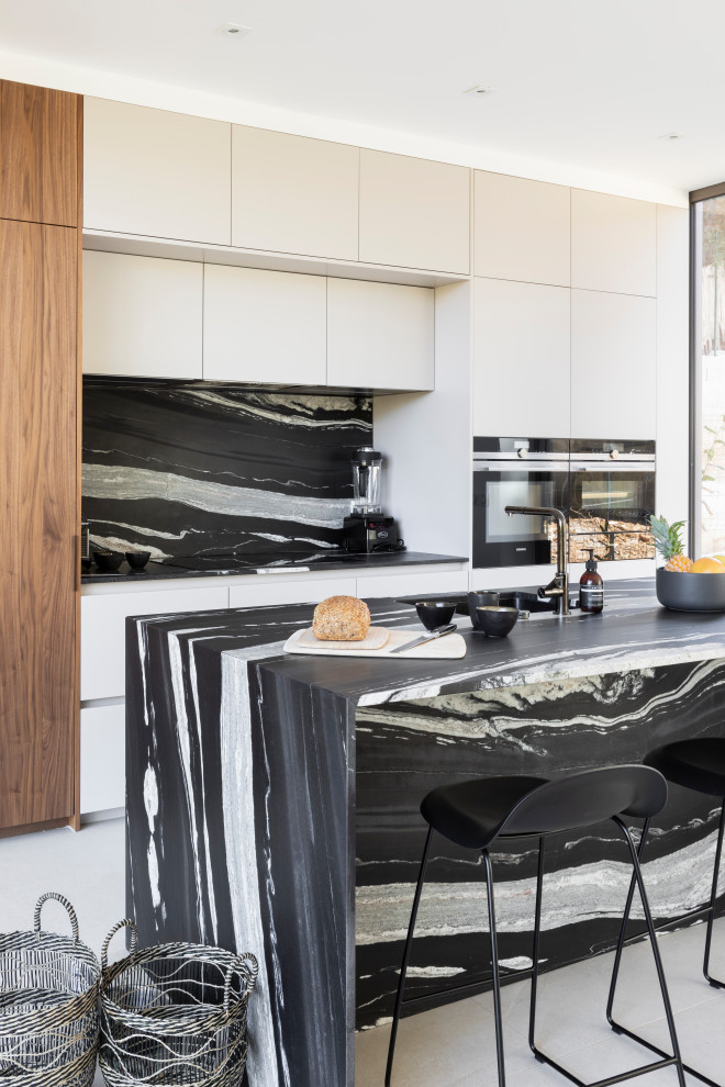 Photo of a large contemporary single-wall kitchen in Paris with an integrated sink, recessed-panel cabinets, white cabinets, granite benchtops, black splashback, granite splashback, panelled appliances, ceramic floors, with island, beige floor and black benchtop.