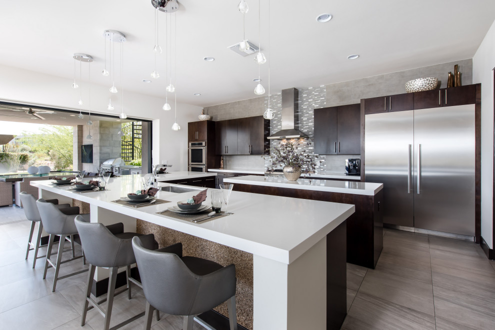 This is an example of a large contemporary l-shaped open plan kitchen in Las Vegas with an undermount sink, dark wood cabinets, solid surface benchtops, stainless steel appliances, multiple islands, grey floor and white benchtop.