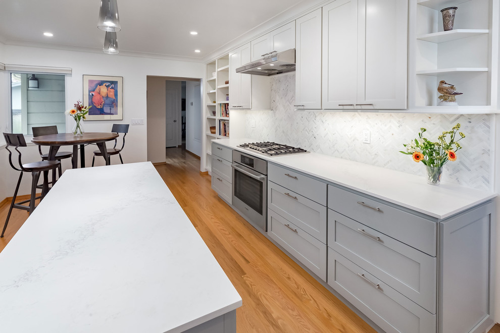 Large contemporary l-shaped eat-in kitchen in Other with a double-bowl sink, shaker cabinets, white cabinets, quartz benchtops, white splashback, mosaic tile splashback, stainless steel appliances, light hardwood floors and with island.