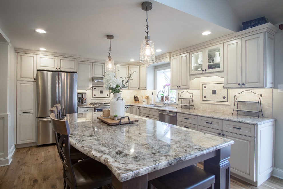 Inspiration for a large transitional l-shaped eat-in kitchen in Philadelphia with an undermount sink, raised-panel cabinets, beige cabinets, granite benchtops, beige splashback, stone tile splashback, stainless steel appliances, medium hardwood floors, with island and brown floor.