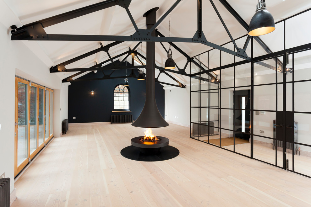Expansive industrial formal open concept living room in Kent with black walls, light hardwood floors, a hanging fireplace, a metal fireplace surround and a wall-mounted tv.