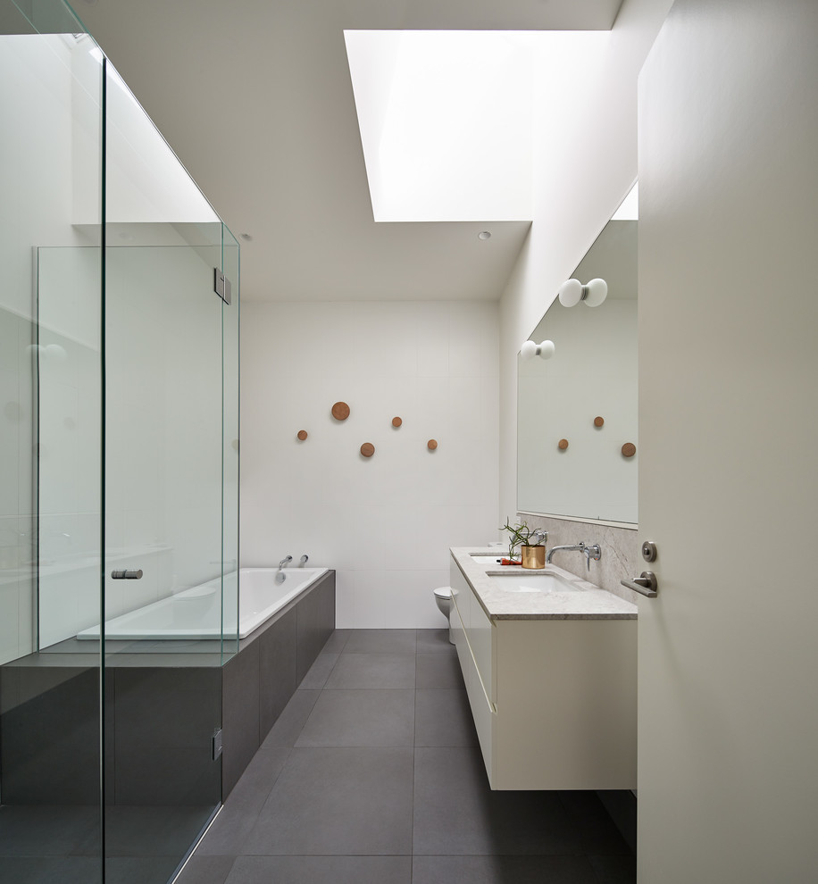 Design ideas for a contemporary master bathroom in Melbourne with flat-panel cabinets, white cabinets, a drop-in tub, white walls, an undermount sink, grey floor and grey benchtops.