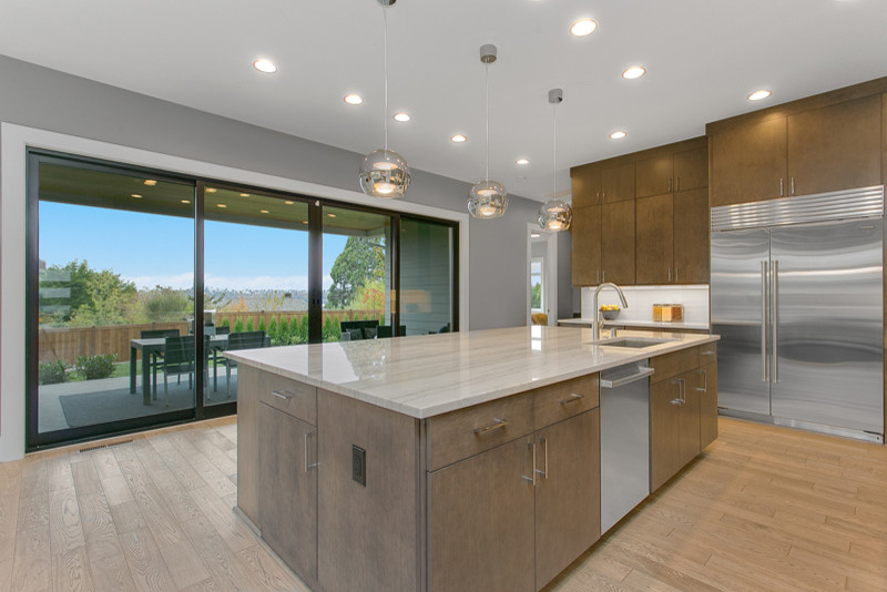 Photo of a large contemporary l-shaped eat-in kitchen in Seattle with an undermount sink, flat-panel cabinets, grey cabinets, quartz benchtops, white splashback, ceramic splashback, stainless steel appliances, light hardwood floors and with island.