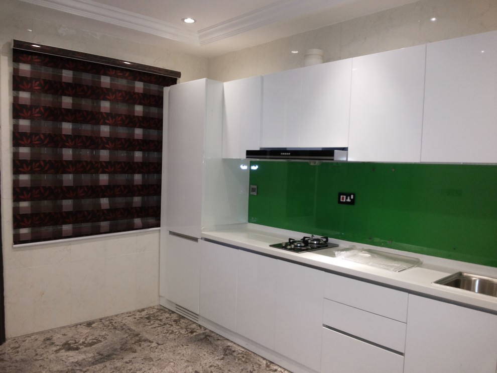 Photo of a modern single-wall separate kitchen in Other with an undermount sink, flat-panel cabinets, white cabinets, solid surface benchtops, green splashback, glass tile splashback, stainless steel appliances and no island.