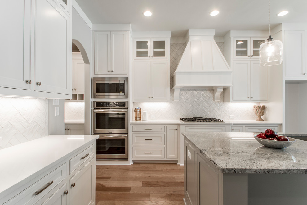 Example of a large transitional u-shaped light wood floor and beige floor eat-in kitchen design in Little Rock with an undermount sink, recessed-panel cabinets, white cabinets, granite countertops, white backsplash, ceramic backsplash, stainless steel appliances, an island and gray countertops