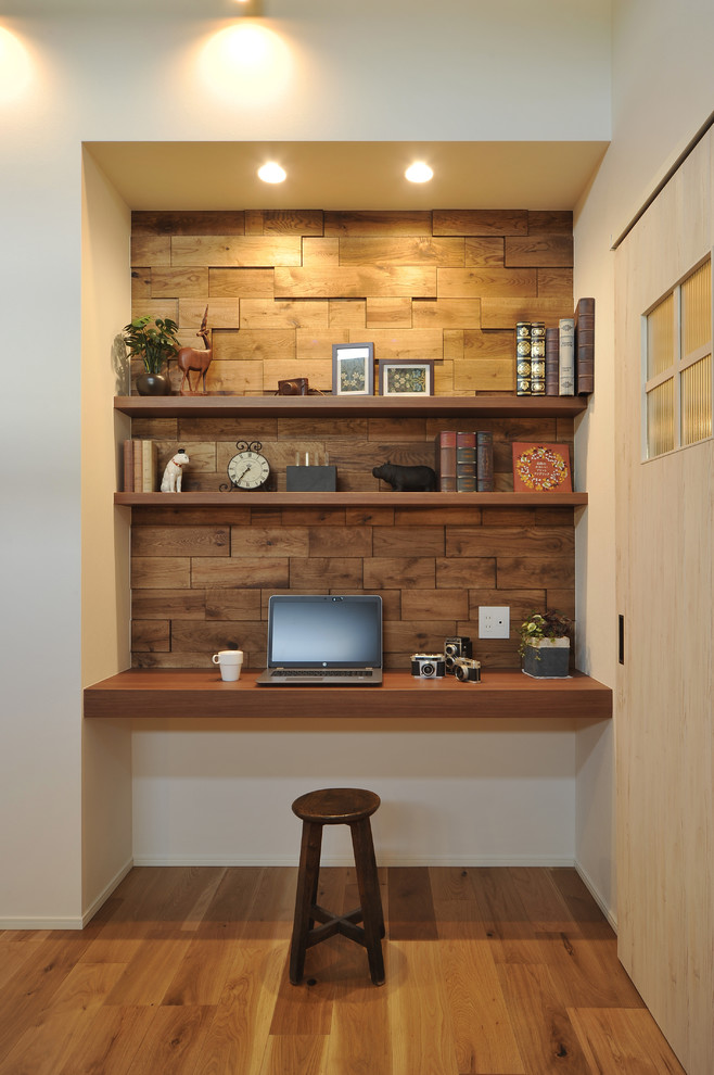 Photo of a country home office in Other with white walls, medium hardwood floors, a built-in desk and brown floor.