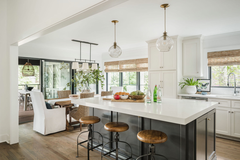 Photo of a mid-sized beach style l-shaped eat-in kitchen in Charlotte with a double-bowl sink, shaker cabinets, white cabinets, quartz benchtops, white splashback, porcelain splashback, stainless steel appliances, light hardwood floors, with island, multi-coloured floor and white benchtop.