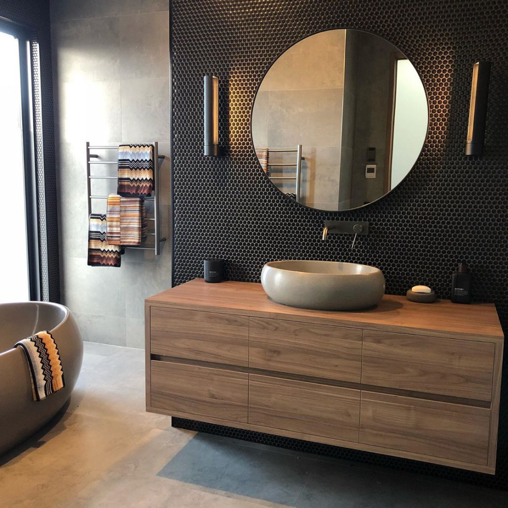 Design ideas for a contemporary bathroom in Other with recessed-panel cabinets, medium wood cabinets, a freestanding tub, black tile, mosaic tile, a vessel sink, wood benchtops, grey floor, brown benchtops, a single vanity and a floating vanity.