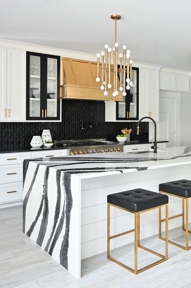 Mid-sized modern l-shaped open plan kitchen in Houston with a farmhouse sink, recessed-panel cabinets, white cabinets, quartz benchtops, black splashback, ceramic splashback, stainless steel appliances, porcelain floors, with island, grey floor and white benchtop.