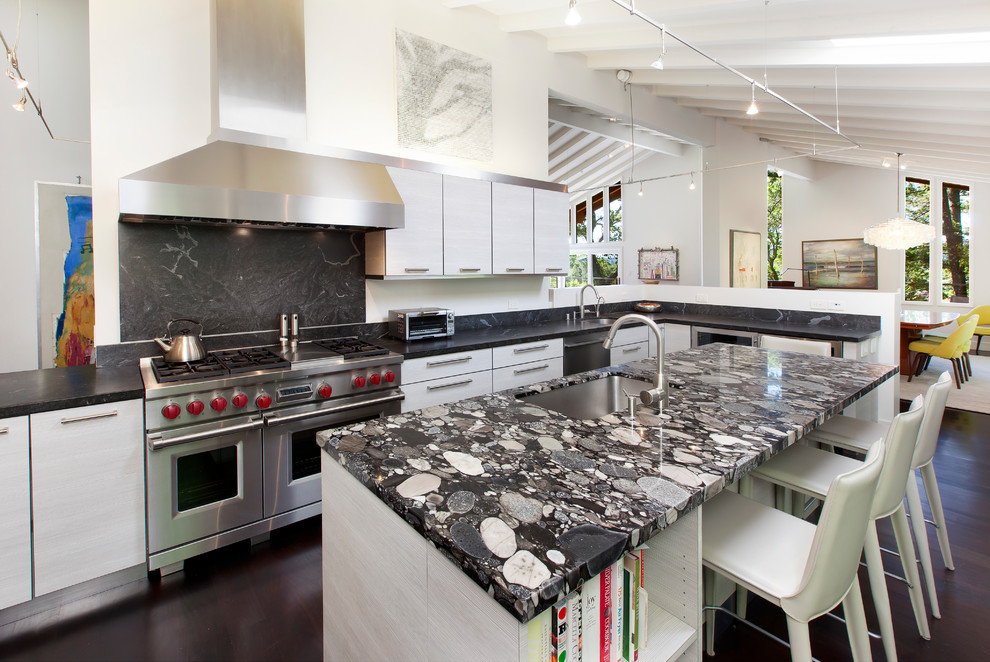 Photo of a large contemporary u-shaped kitchen in San Francisco with flat-panel cabinets, grey cabinets, granite benchtops, black splashback, stone slab splashback, stainless steel appliances, dark hardwood floors, with island, black benchtop, an undermount sink and brown floor.