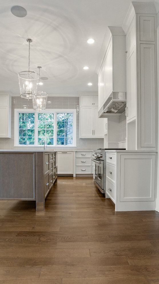 This is an example of a mid-sized modern kitchen in Chicago with beaded inset cabinets, medium wood cabinets, solid surface benchtops, white splashback, stone tile splashback, stainless steel appliances, medium hardwood floors, with island, brown floor and white benchtop.