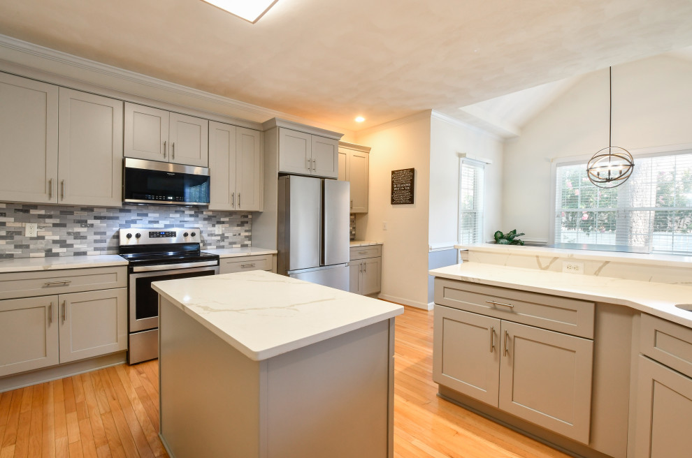 This is an example of a large contemporary u-shaped open plan kitchen in DC Metro with a drop-in sink, shaker cabinets, grey cabinets, quartz benchtops, stainless steel appliances, with island and white benchtop.