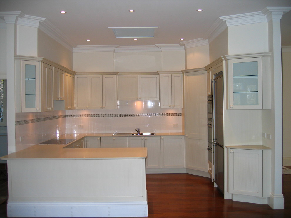 Design ideas for a mid-sized contemporary u-shaped eat-in kitchen in Wollongong with a drop-in sink, recessed-panel cabinets, beige cabinets, quartz benchtops, white splashback, ceramic splashback, stainless steel appliances and medium hardwood floors.