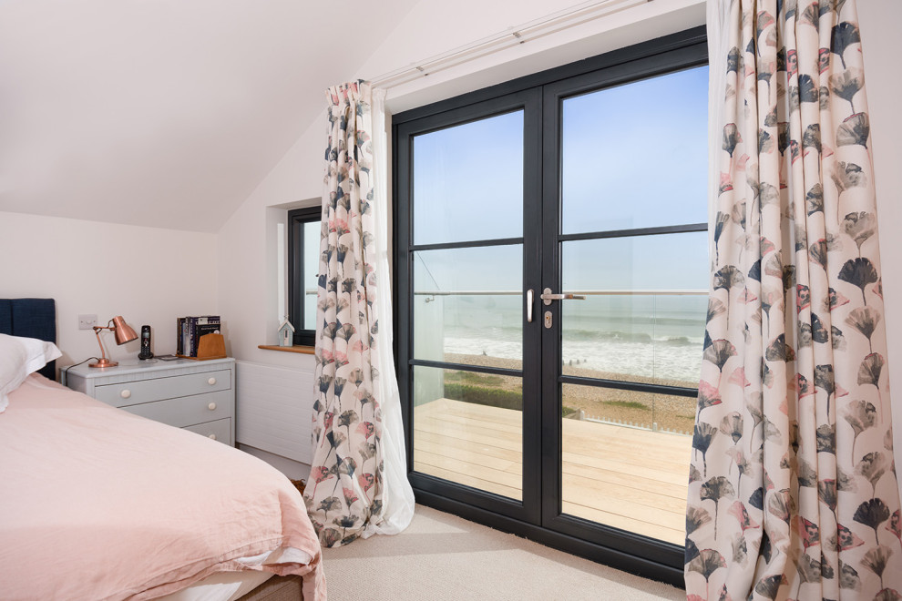 Large beach style guest bedroom in Hertfordshire with beige walls, carpet, beige floors and feature lighting.