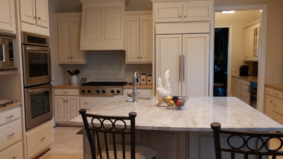 Photo of a mid-sized traditional kitchen in Atlanta with raised-panel cabinets, white cabinets, quartz benchtops, porcelain splashback, panelled appliances, limestone floors and with island.