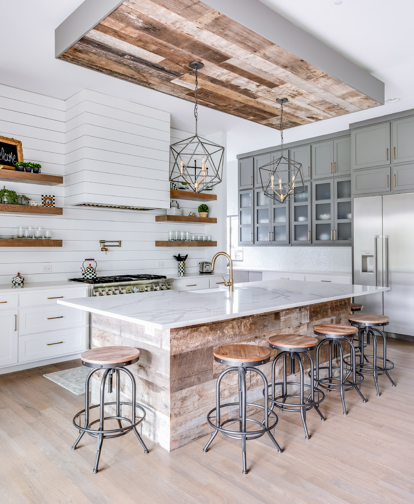 Design ideas for a country l-shaped kitchen in Dallas with a farmhouse sink, shaker cabinets, white cabinets, stainless steel appliances, light hardwood floors, with island, beige floor and white benchtop.