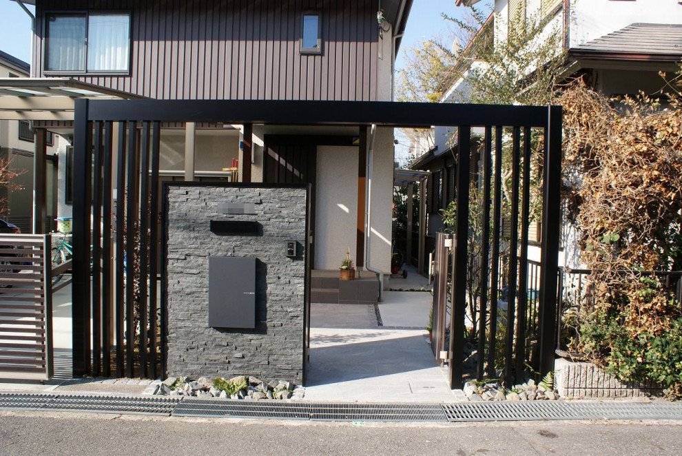 Mid-sized front yard full sun driveway in Kobe with with a gate, natural stone pavers and a metal fence for winter.