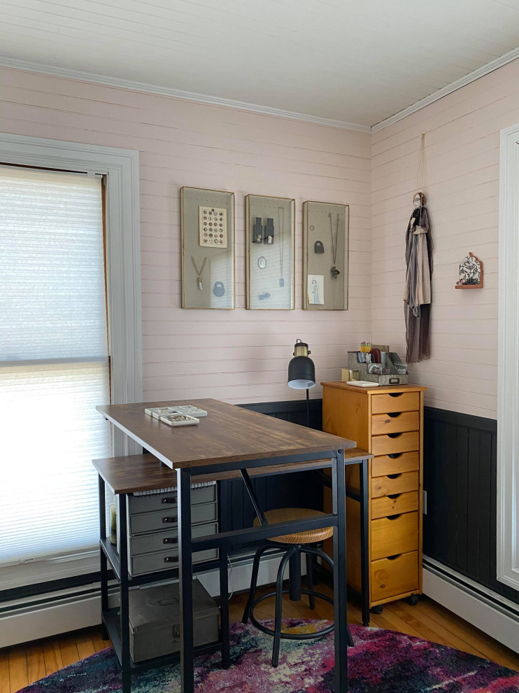 Inredning av ett industriellt litet hemmastudio, med rosa väggar, mellanmörkt trägolv och ett fristående skrivbord
