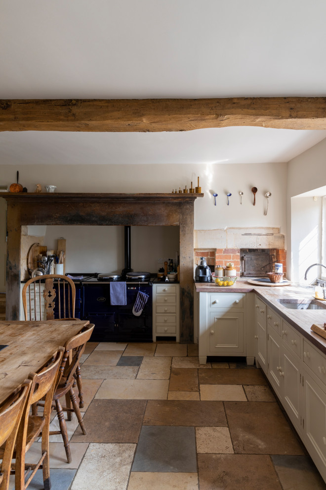 This is an example of a rural l-shaped kitchen/diner in Gloucestershire with a submerged sink, recessed-panel cabinets, beige cabinets, wood worktops, black appliances, a breakfast bar, multi-coloured floors, brown worktops and exposed beams.