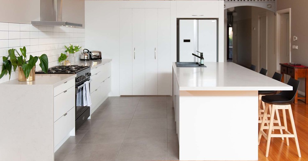 Design ideas for a large modern galley kitchen pantry in Melbourne with a double-bowl sink, open cabinets, white cabinets, solid surface benchtops, white splashback, subway tile splashback, black appliances, cement tiles, with island, grey floor and white benchtop.