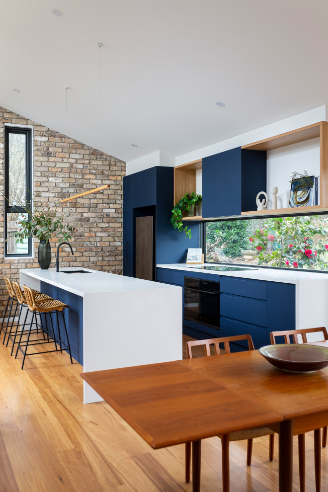 Immagine di una cucina minimal di medie dimensioni con lavello sottopiano, ante blu, top in quarzo composito, paraspruzzi a finestra, elettrodomestici neri, pavimento in legno massello medio e top bianco