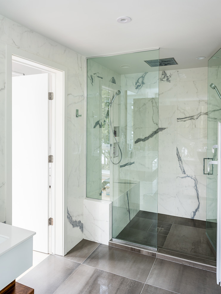 This is an example of a mid-sized modern master bathroom in Burlington with flat-panel cabinets, brown cabinets, a freestanding tub, an alcove shower, a one-piece toilet, white tile, marble, white walls, ceramic floors, a drop-in sink, granite benchtops, grey floor, a hinged shower door and white benchtops.