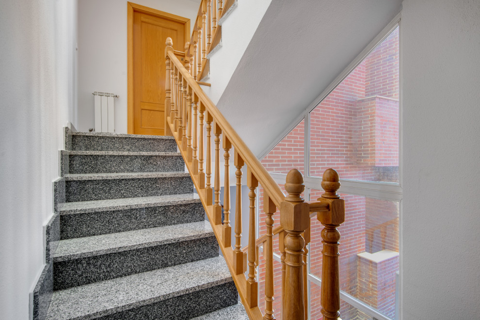 This is an example of an expansive traditional limestone u-shaped staircase in Madrid with limestone risers and wood railing.