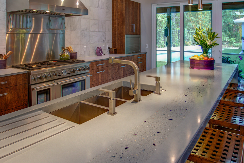 Photo of a large contemporary l-shaped open plan kitchen in Tampa with a triple-bowl sink, flat-panel cabinets, medium wood cabinets, concrete benchtops, stone tile splashback, stainless steel appliances, porcelain floors and with island.