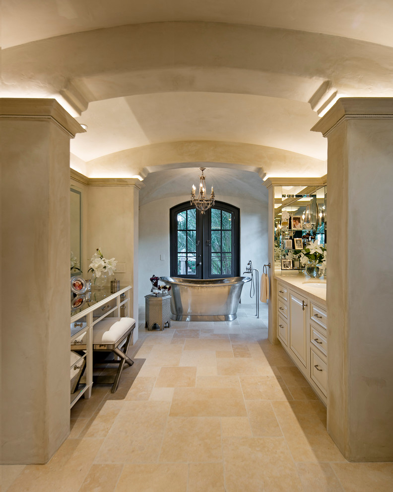 Inspiration for a large mediterranean master bathroom in Santa Barbara with recessed-panel cabinets, beige cabinets, a freestanding tub, a curbless shower, a one-piece toilet, beige tile, limestone, beige walls, limestone floors, an undermount sink, limestone benchtops, beige floor and an open shower.