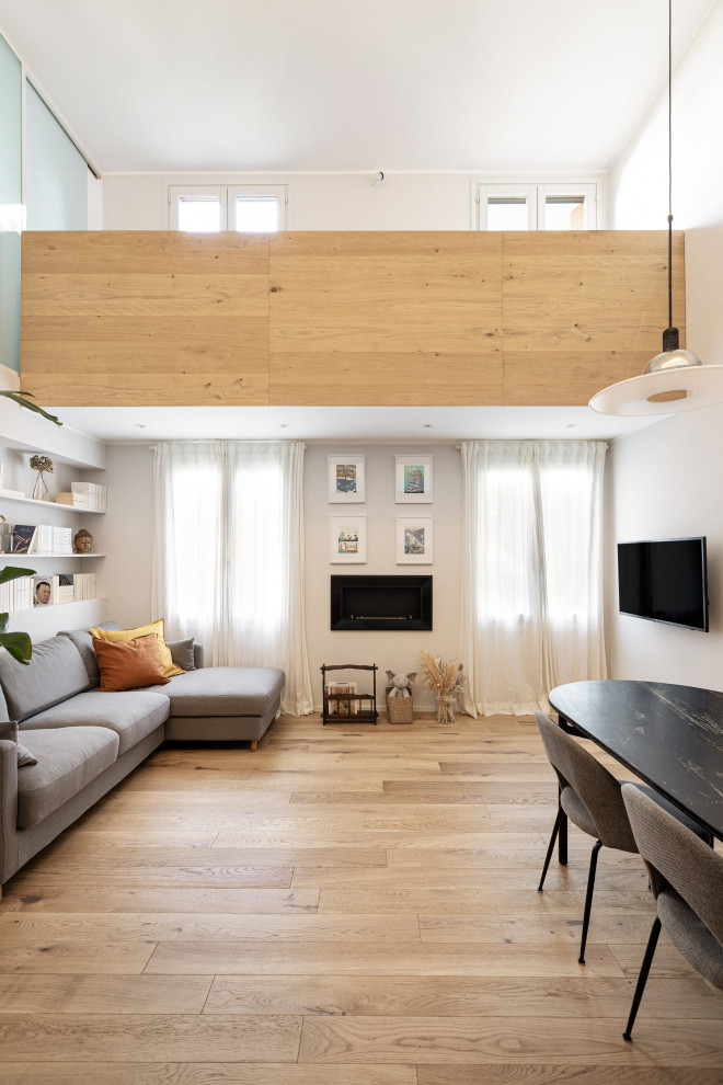 Foto på ett stort nordiskt allrum med öppen planlösning, med vita väggar, ljust trägolv, en bred öppen spis och en väggmonterad TV