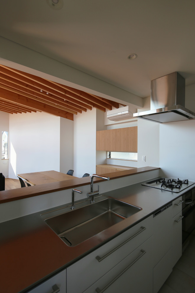Design ideas for a small asian single-wall separate kitchen in Tokyo with an integrated sink, beaded inset cabinets, white cabinets, stainless steel benchtops, white splashback, glass sheet splashback, black appliances, light hardwood floors, with island and beige floor.