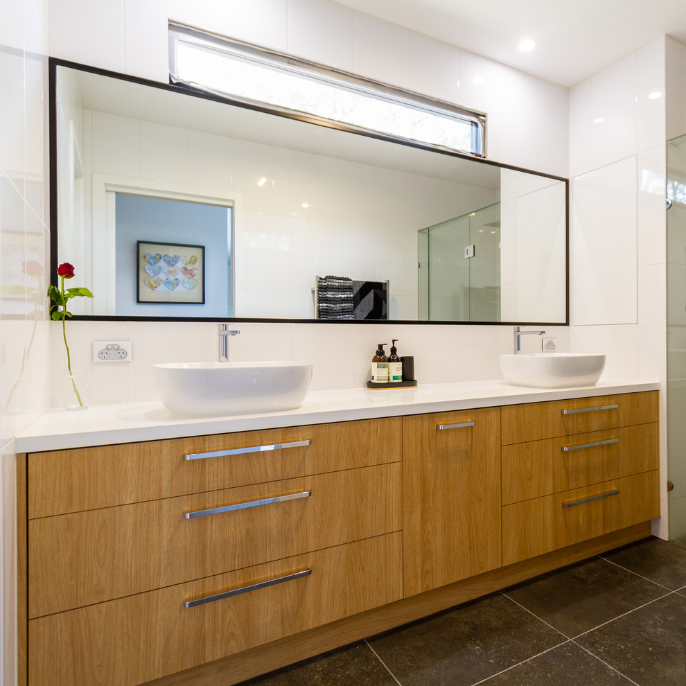 Photo of a large master bathroom in Melbourne with flat-panel cabinets, medium wood cabinets, an alcove shower, white tile, porcelain tile, white walls, porcelain floors, a vessel sink, engineered quartz benchtops, grey floor, a hinged shower door and white benchtops.