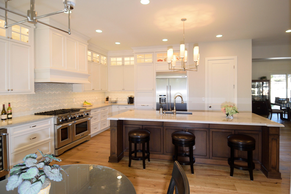 Inspiration for a mid-sized transitional l-shaped medium tone wood floor eat-in kitchen remodel with an undermount sink, recessed-panel cabinets, dark wood cabinets, granite countertops, gray backsplash, glass tile backsplash, stainless steel appliances and an island