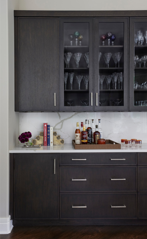 Photo of a mid-sized eclectic single-wall home bar in Grand Rapids with recessed-panel cabinets, black cabinets, quartz benchtops, white splashback, engineered quartz splashback, dark hardwood floors, brown floor and white benchtop.