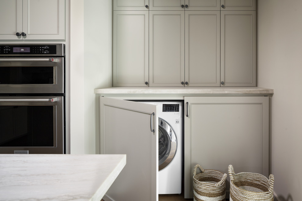 Inspiration for a small arts and crafts galley utility room in Houston with shaker cabinets, grey cabinets, quartzite benchtops, white walls, light hardwood floors, a concealed washer and dryer, brown floor and white benchtop.