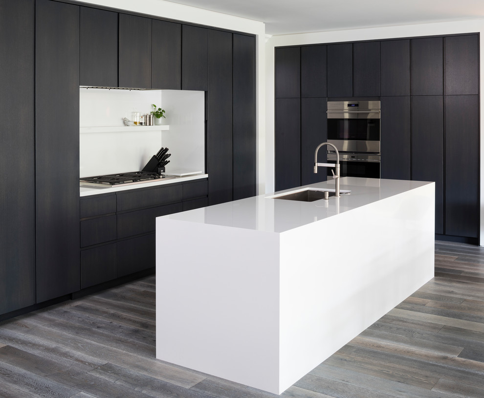 Photo of a mid-sized contemporary l-shaped eat-in kitchen in Minneapolis with flat-panel cabinets, panelled appliances, medium hardwood floors, with island, grey floor, an undermount sink, black cabinets and quartzite benchtops.