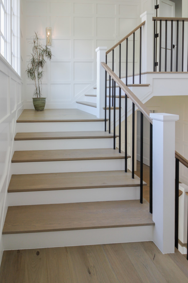 Пример оригинального дизайна: большая п-образная деревянная лестница в стиле неоклассика (современная классика) с деревянными ступенями, деревянными перилами и панелями на стенах